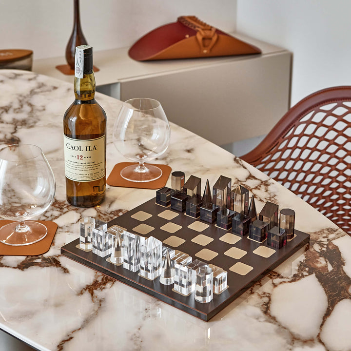 Cigarillo bottle, glasses, and a chess set on a marble table.
