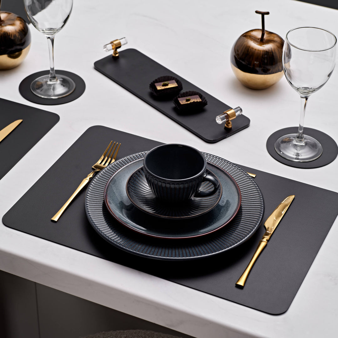 Dining table setting with black plates, gold cutlery, and decorative items on a white surface.