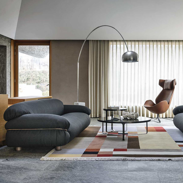Modern living room with a gray sofa, wooden armchair, and decorative rug.