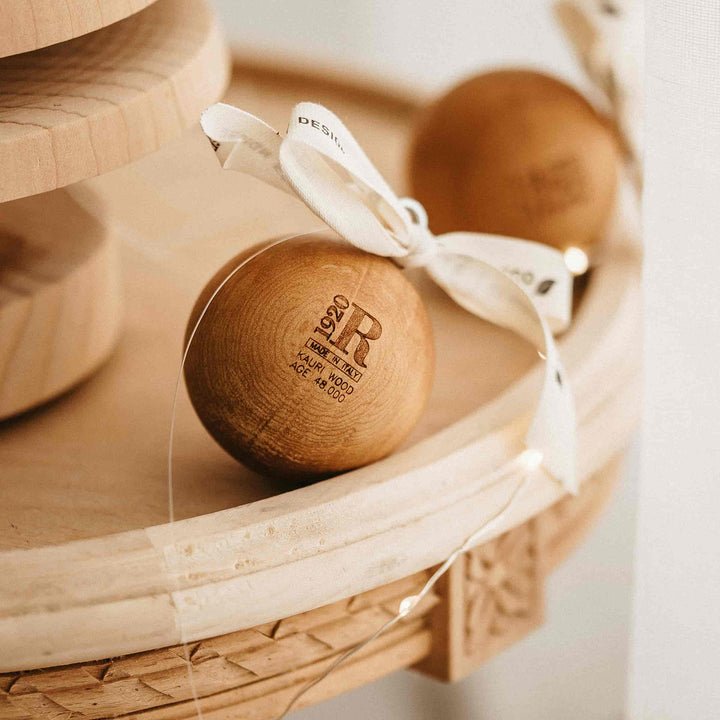Wooden ball with a white ribbon on a woven surface, featuring a brand logo.