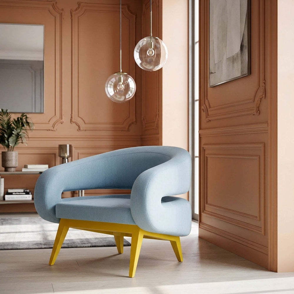 Light blue ROCHE armchair by Adrenalina with curved upholstered arms and yellow legs in a sunlit, terracotta-panelled room.