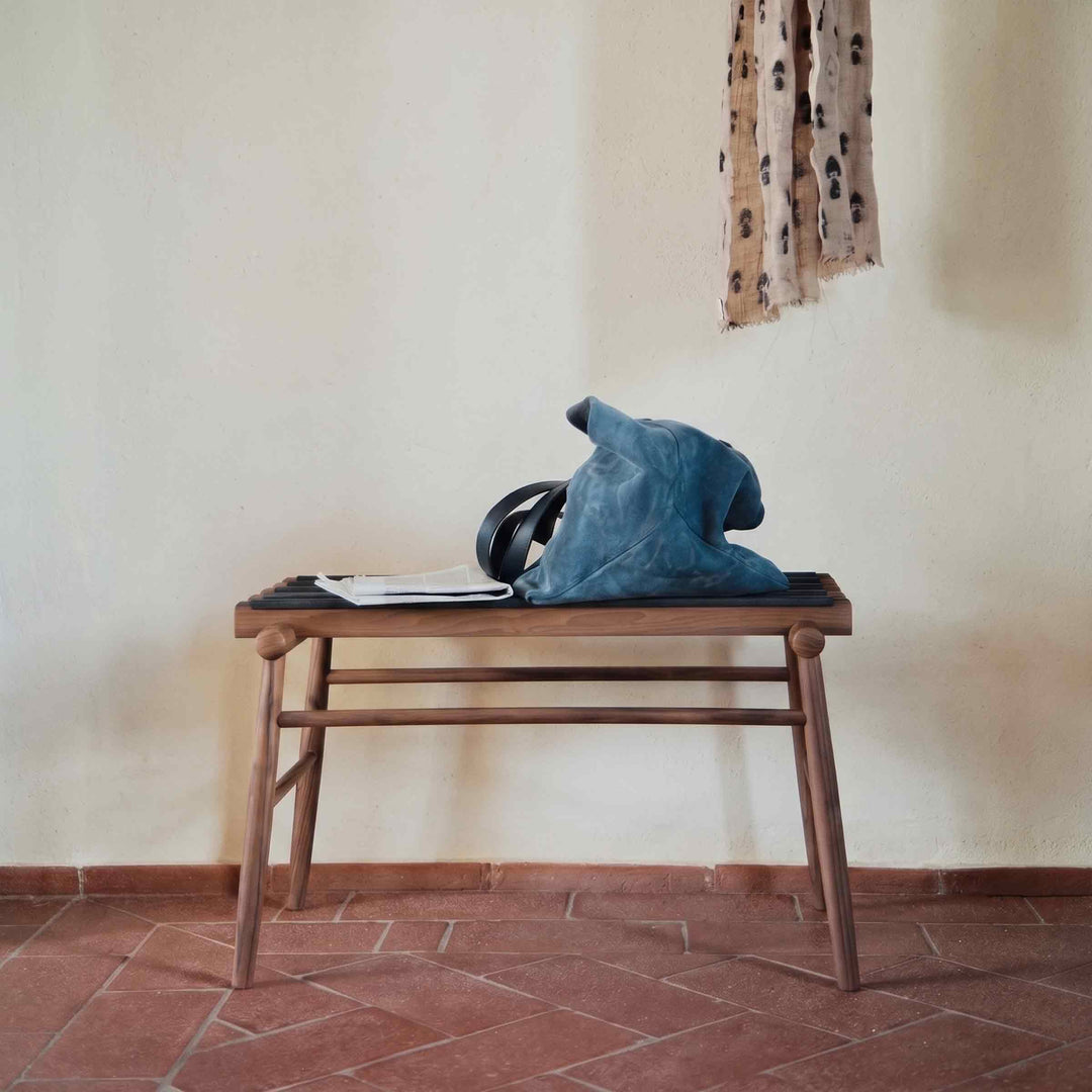 Lodi walnut luggage stand by Internoitaliano with dark support straps, holding a blue bag on a terracotta floor.