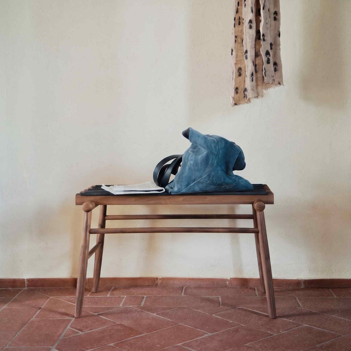 Lodi walnut luggage stand by Internoitaliano with dark support straps, holding a blue bag on a terracotta floor.