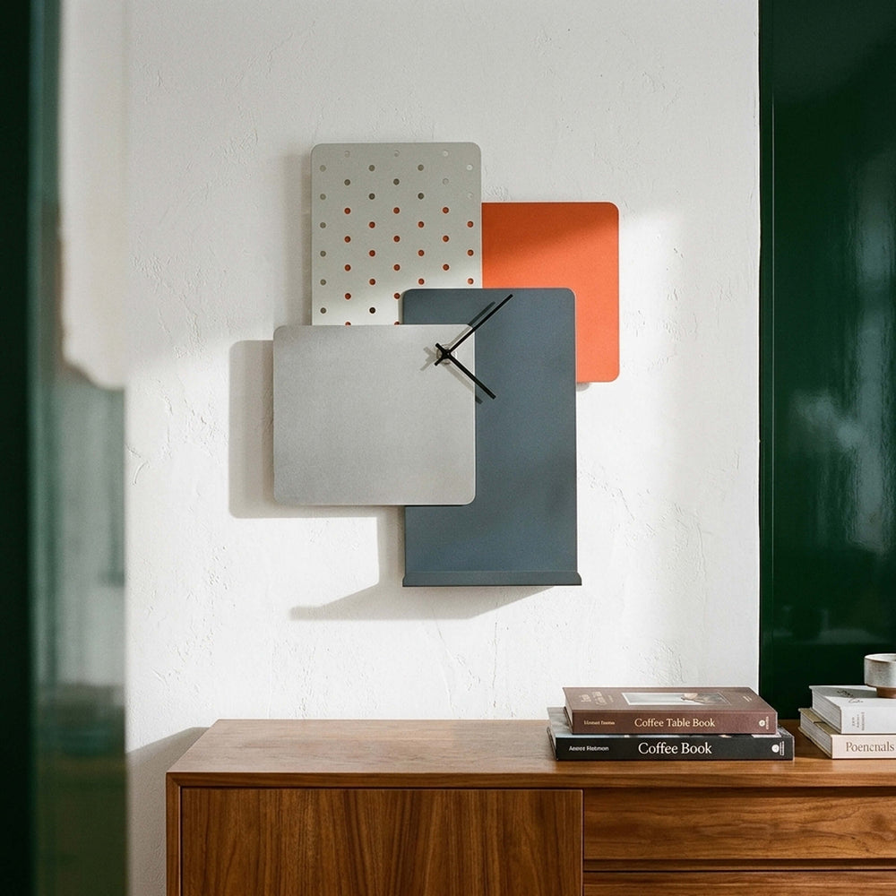 Giacopini CLOOK mirror wall clock with overlapping grey, orange and perforated panels above a wooden sideboard