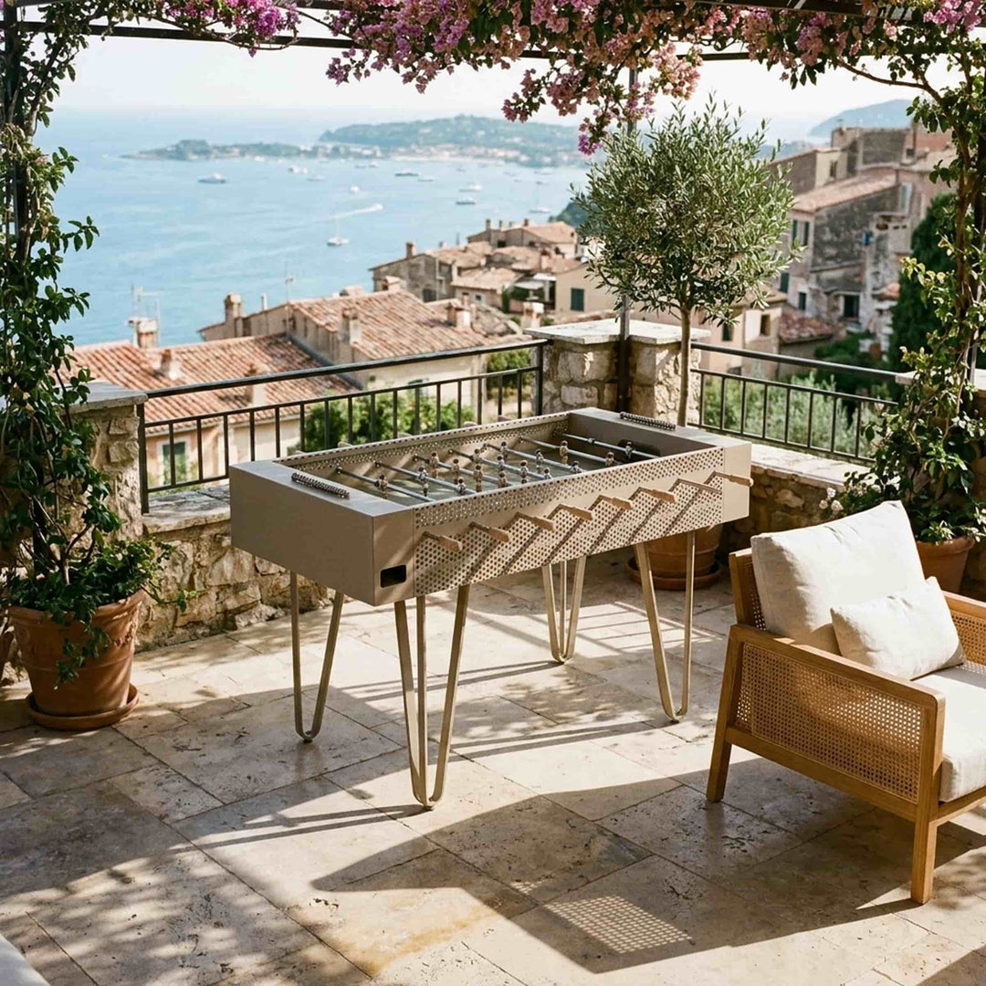 Giacopini JOIE sand-coloured foosball table on a flower-covered terrace overlooking the sea