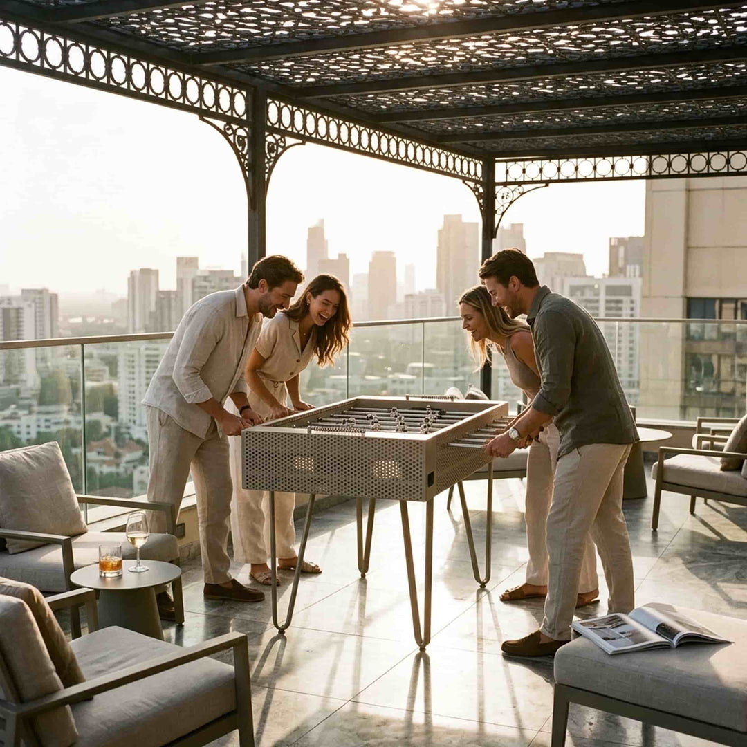 Four people playing at a Giacopini JOIE sand-coloured foosball table on a rooftop terrace