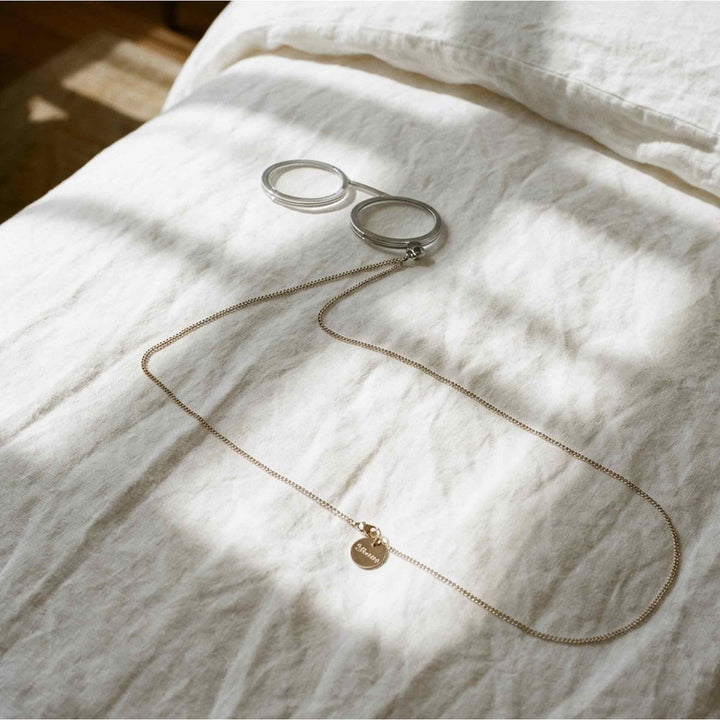 Fassamano Capri reading glasses with round translucent frames and a fine neck chain on white linen