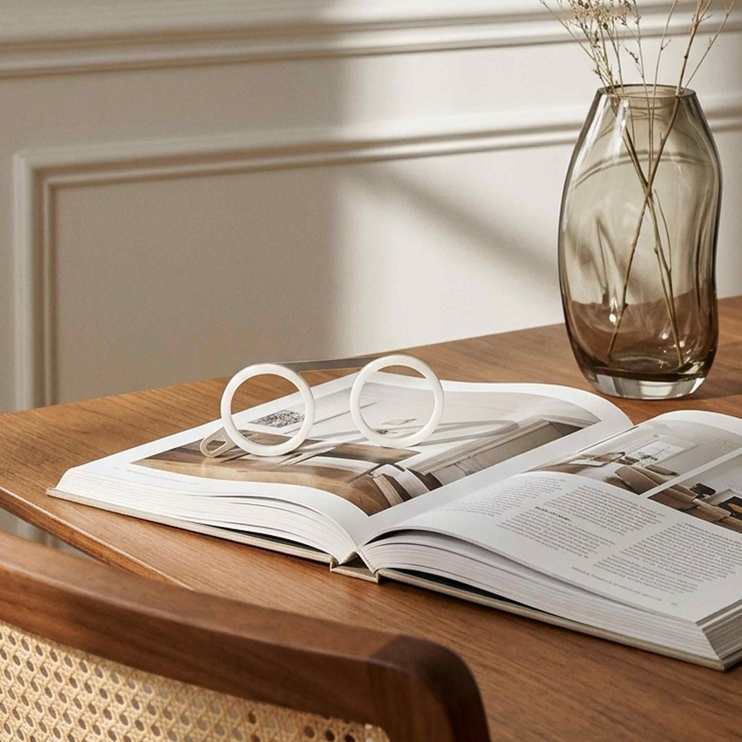 Fassamano reading glasses with round white frames resting on an open magazine on a wooden table