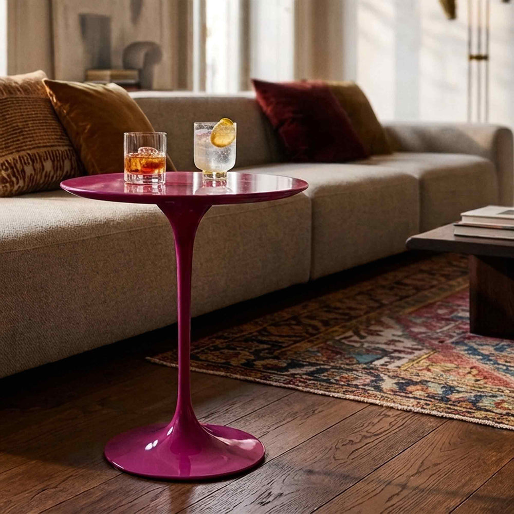 Pink Saarinen side table by Giovannetti with a round top and tulip pedestal base, holding two drinks beside a beige sofa.