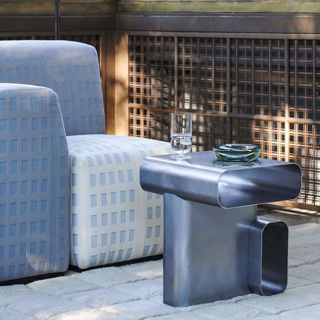 Metallic Soft Corners side table by Cassina with curved edges, beside a pale blue upholstered armchair.