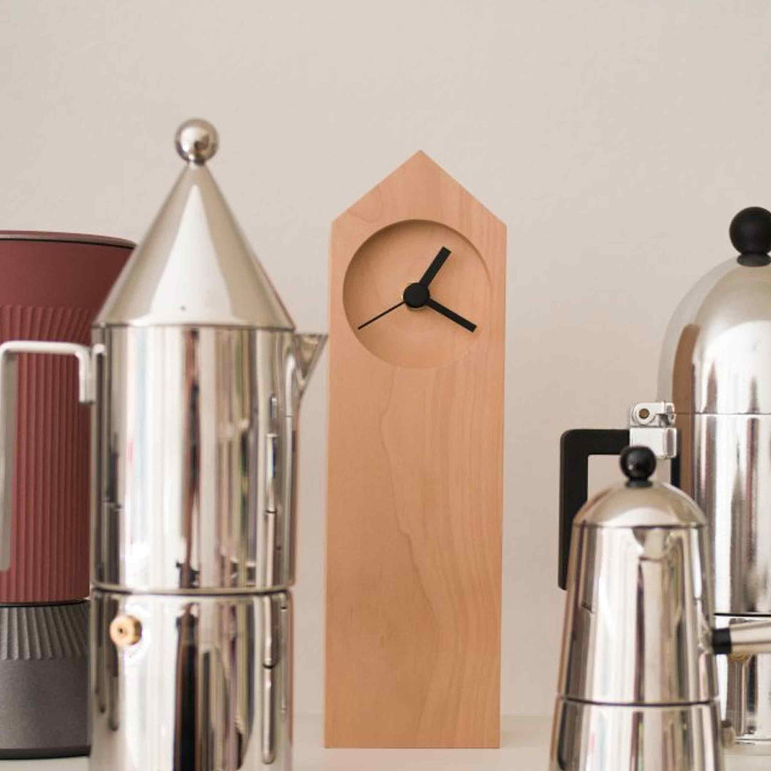 Osio table clock by Internoitaliano with a tall, house-shaped wooden body and black hands, displayed among metal coffee makers.
