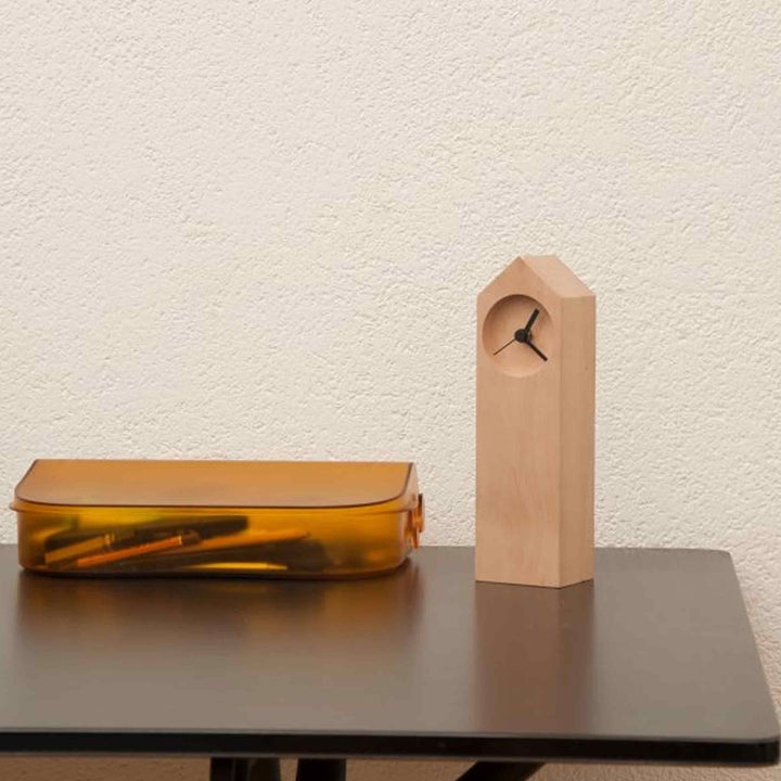 Osio wooden table clock by Internoitaliano on a dark tabletop beside an amber storage case.
