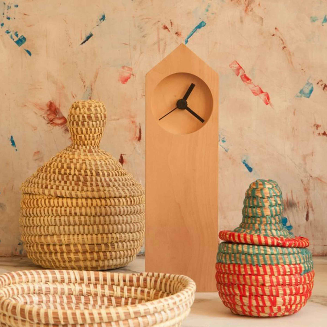 Osio wooden table clock by Internoitaliano with a recessed round face and black hands, displayed among woven baskets.