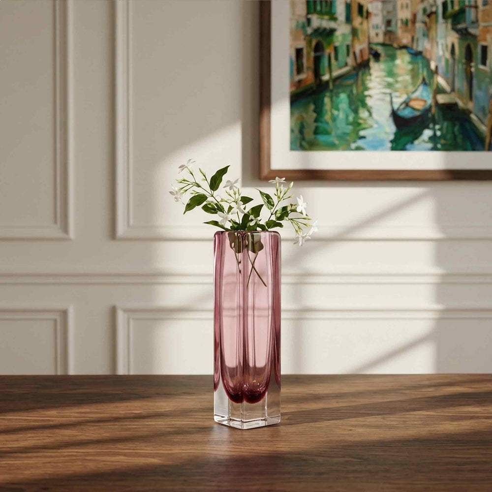 Tall amethyst-coloured square glass vase by Alessandro Mandruzzato holding white flowers on a wooden table beneath a painting